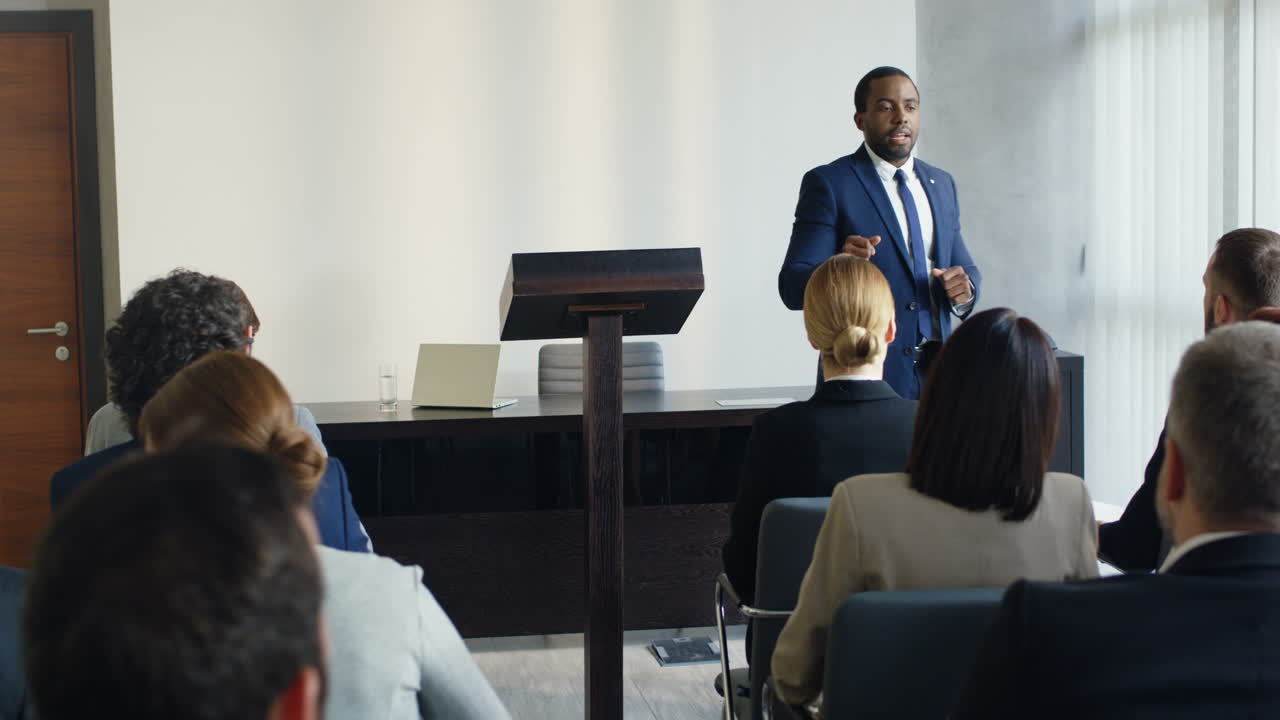 African American young businessman wearing formal clothes speaking at the conference in front of the many people