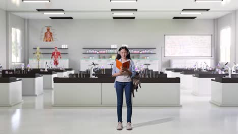 cuerpo lleno de estudiante adolescente asiática con una mochila sosteniendo y leyendo un libro mientras estaba de pie en el laboratorio de ciencias