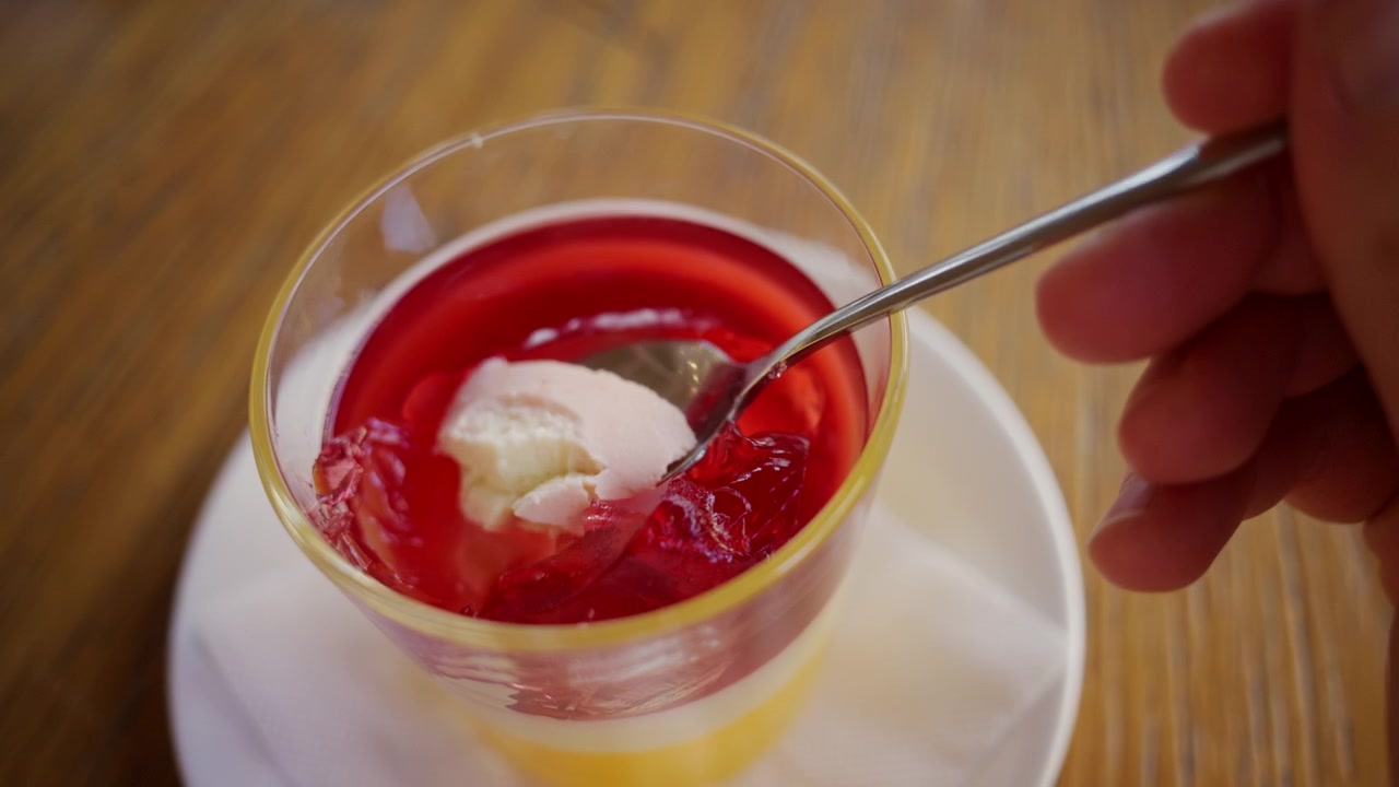 Primo piano di un cucchiaio che solleva un pezzo di gelatina di frutta rosso vivo da una coppetta da dessert di plastica trasparente.