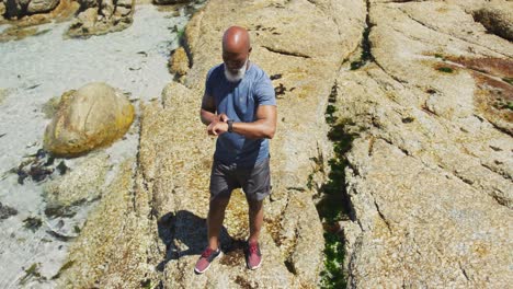 senior african american man exercising using smartwatch on rocks by the sea