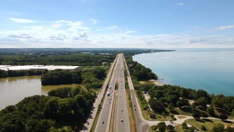 Aerial-view-of-cars-driving-on-a-highway-next-to-a-beautiful-emerald-lake