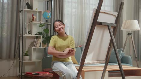 asian artist girl holding paintbrush crossing his arm and smiling after finish painting a girl on the canvas