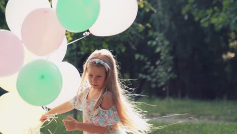 little girl plays spinning with balloons in her hands in the park. a child in a dress with colorful balloons