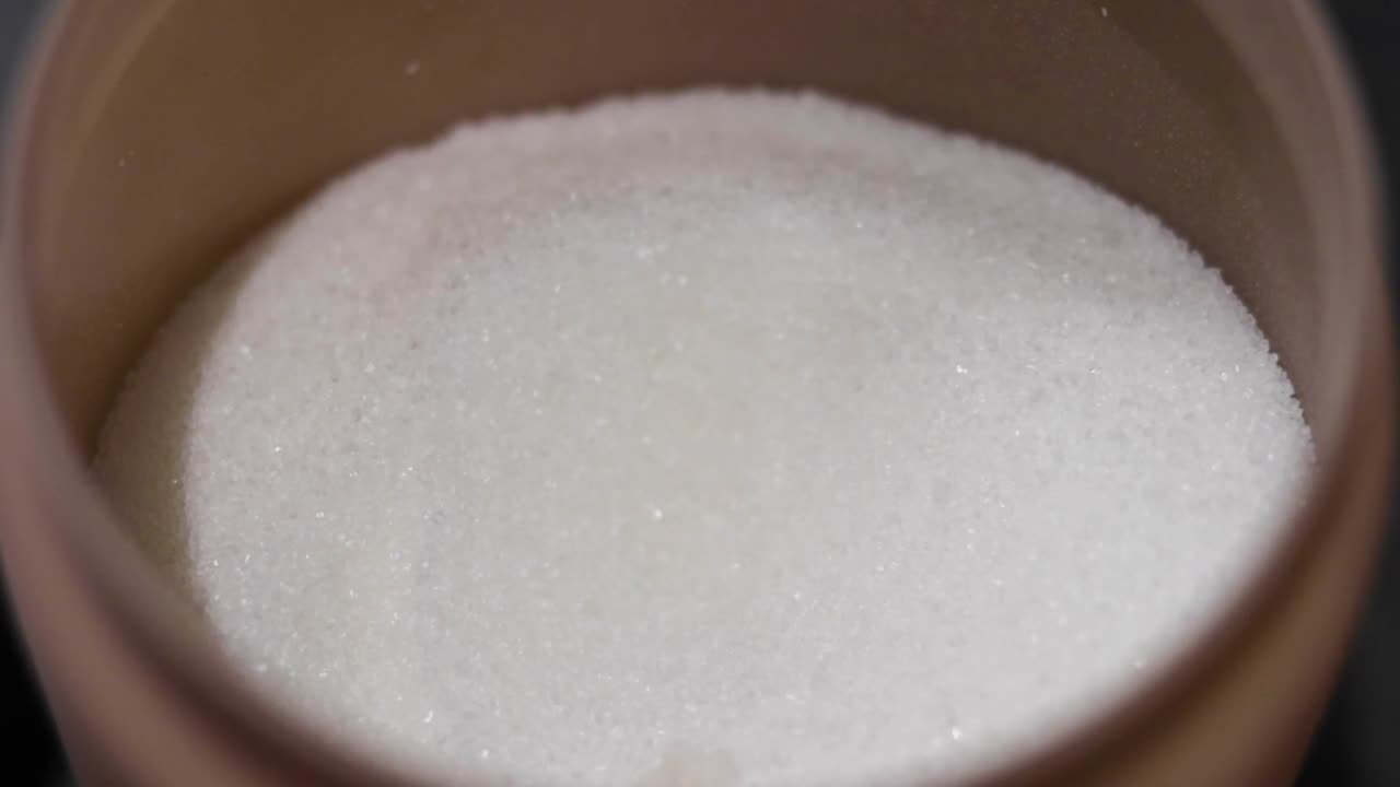 persona tomando una cuchara llena de azúcar de un azucarero