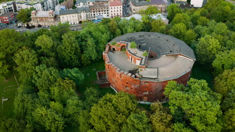 Aerial-view-of-alone,-rounded,-brick-fortress-in-forest-in-Krakow,-Poland