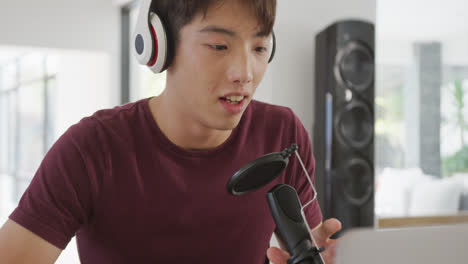 asian boy wearing headphones speaking on professional microphone to record audio podcast at home