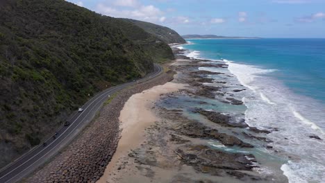 Motorcycles-and-cars-drive-on-famous-Great-Ocean-Road-next-to-beach,-Victoria,-Australia