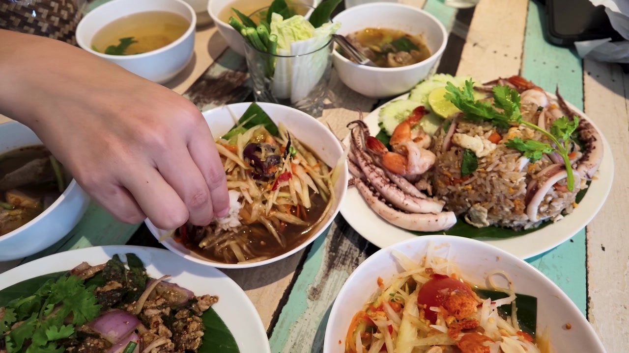 Pengambilan gambar dari atas seseorang mencelupkan nasi ketan ke dalam salad pepaya di Bangkok, Thailand.