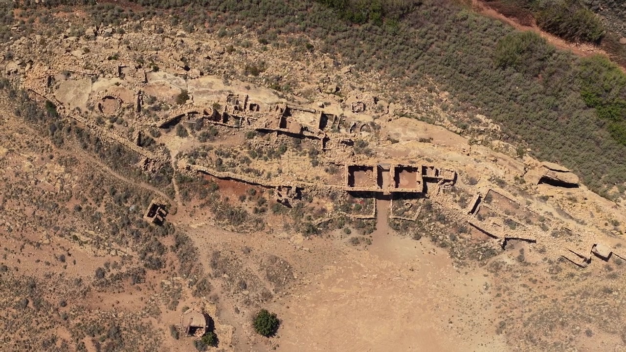 A top down drone shot explores the decaying stone walls of a remote historical site. The vertical perspective highlights the intricate textures of the ruins against the rugged high desert terrain.