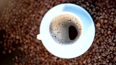 a white coffee mug is standing on a pile of roasted coffee beans