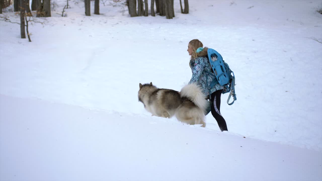mujer joven con mochila camina con perro grande, escena de invierno nevada, cámara lenta