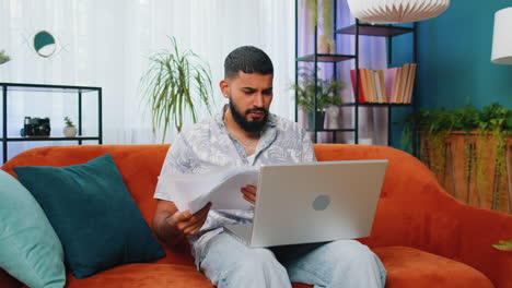 Stressed-Indian-man-looking-at-unpaid-bank-debt-loan,-doing-paperwork,-planning-budget,-throws-bills