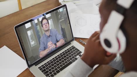 African-american-businessman-sitting-at-desk-using-laptop-having-video-call-with-male-colleague