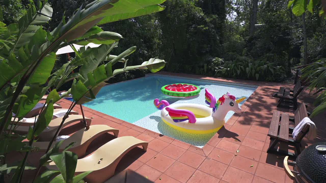 Pool at jungle lodge in Misiones, Argentina features unicorn and strawberry floats, terracotta tiles, and lush greenery—capturing playful leisure in the heart of the Selva Misionera