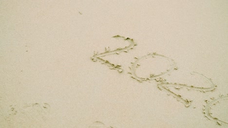 woman hand writes the number 2020 on the sand for new year's eve