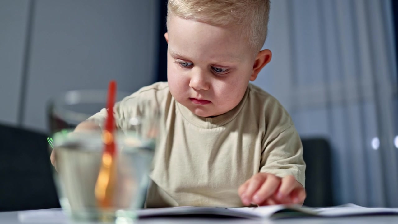 Un bambino è seduto a un tavolo a casa e disegna con i colori. Il bambino si sviluppa e impara l'arte. Il bambino disegna con i colori e acquisisce entusiasmo per il futuro. Il bambino è un futuro artista.