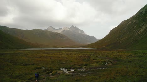 male walking in the nature with a big backpack exploring the beautiful green nature of scotland between the high sky mountains on a cloudy day