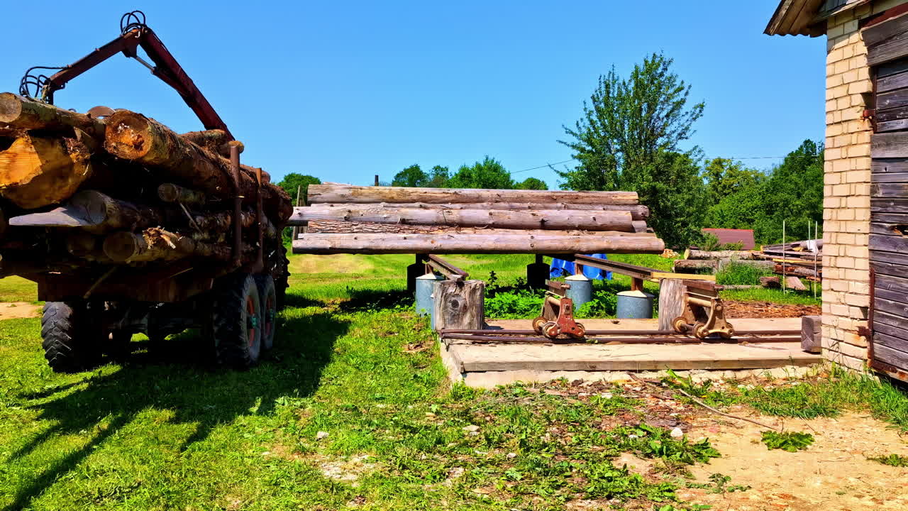 Long trailer with stacked logs in residential backyard garden ready for transport removal