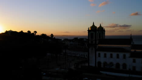 Aerial-view-of-Nosso-Senhor-do-Bonfim-church-back-side,-the-neighbourhood-and-the-ocean-at-background,-at-sunset,-Salvador,-Bahia,-Brazil