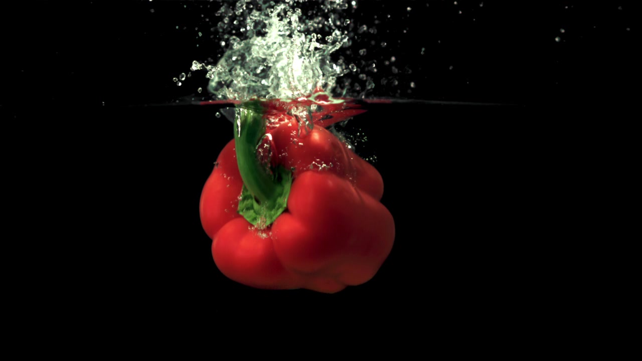Červená paprika stříkající do vody ve zpomaleném záběru