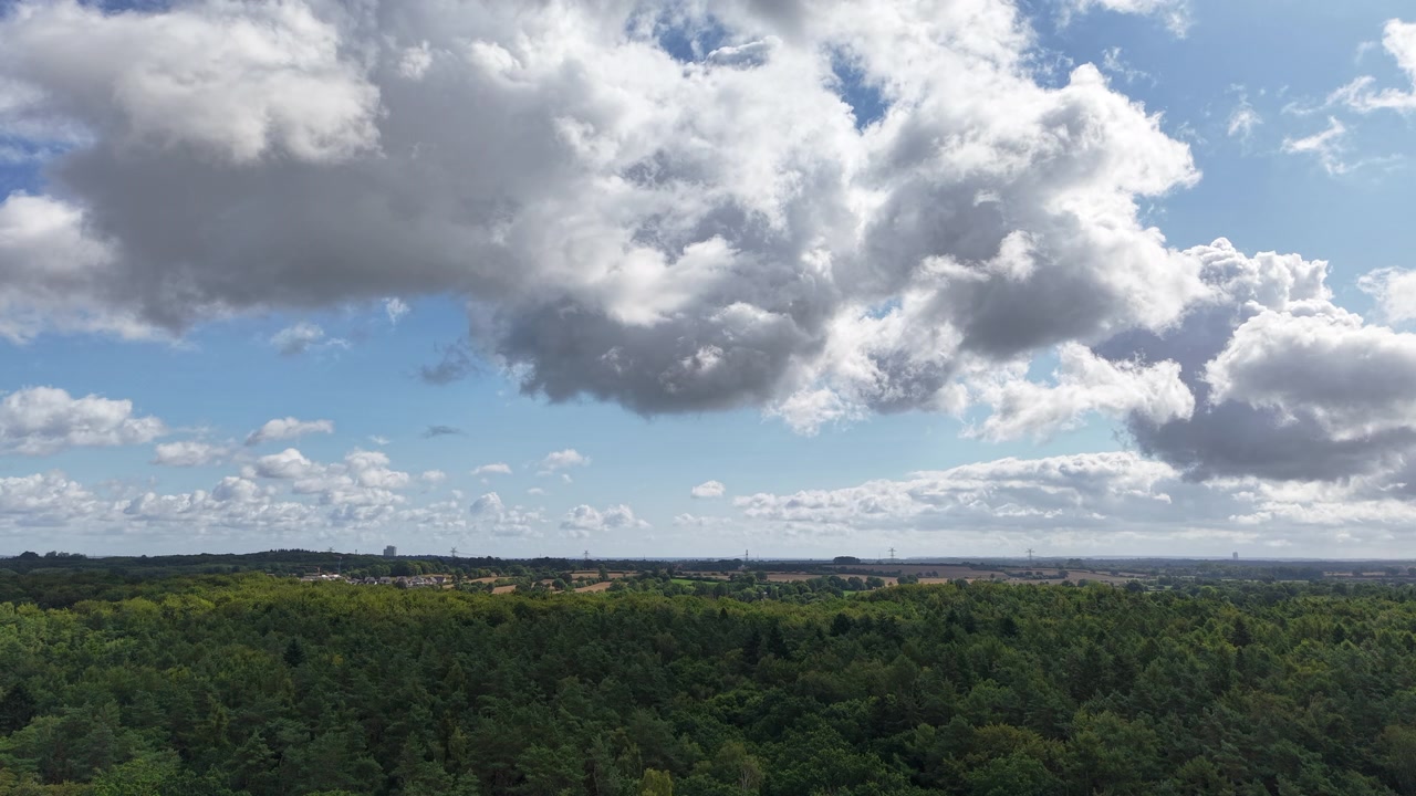 A view of dramatic clouds drifting over a vast green forest landscape beneath a blue sky, capturing the beauty of nature, changing weather, and peaceful wilderness from above.