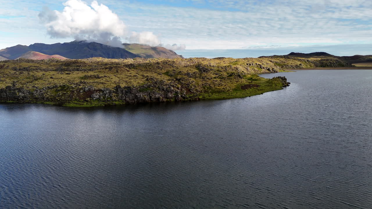 Aerial view of Selvallafoss and Selvallavatn on the Snæfellsnes Peninsula showing calm lake water mossy lava fields and distant mountains under bright clouds in a pristine Icelandic volcanic landscape