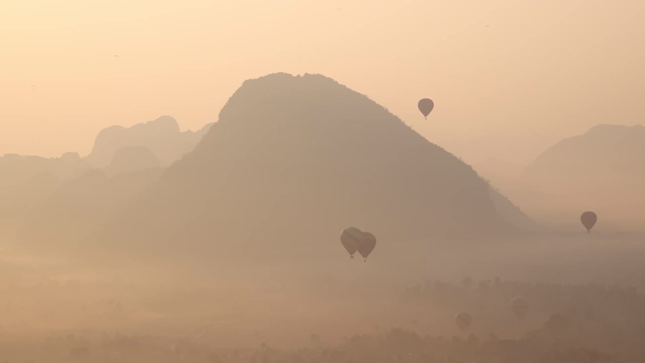 hot air balloons at sunrise in foggy valley in Vang Vieng, the adventure capital of Laos