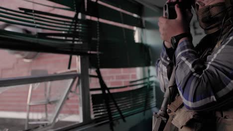 Military-Contractor-With-Spotting-Scope-Rifle-and-Tactical-Camo-Gear-Surveillance-Broken-Window-Abandoned-building