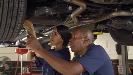 mecánico y aprendiz trabajando juntos debajo de un coche