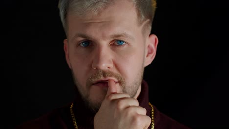 confident bearded man in stylish clothing sensually touching lips with finger on black background