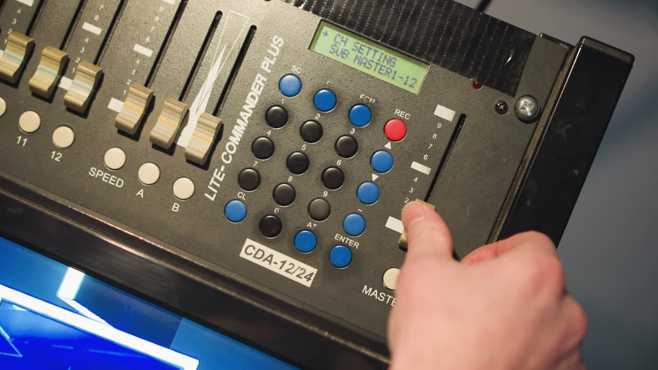 Person adjusting settings on digital lighting control panel with hand, focusing on sliders and buttons, working in a studio or lighting environment, controlling light levels and settings for production