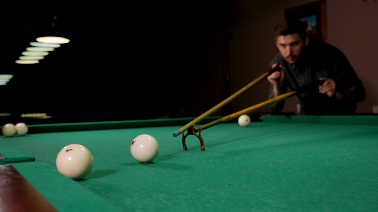 Een man die pool speelt in een donkere bar en probeert de bal in de pocket te stoten