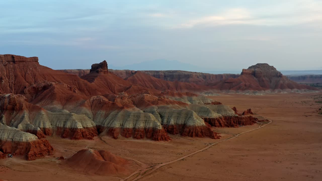 una hermosa foto aérea de un dron de una impresionante escena desértica con arena naranja y grandes formaciones rocosas rojas y blancas con un pequeño camino de tierra durante una cálida tarde de verano al atardecer