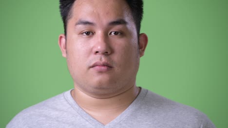 young handsome overweight asian man against green background