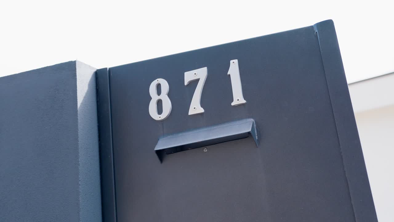 Dark gate with silver 871 house number mounted on it under bright daylight