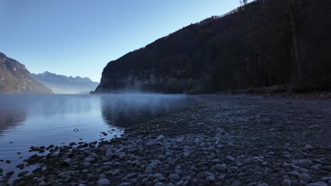 Pebble stones rocks shore Walensee Lake Walen Switzerland morning mist haze over water surface