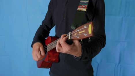 close-up of an unrecognizable person playing the ukele in a room with a blue background