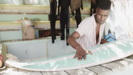 hombre afroamericano preparando tabla de surf en el mostrador de alquiler de surf cabaña de playa, cámara lenta