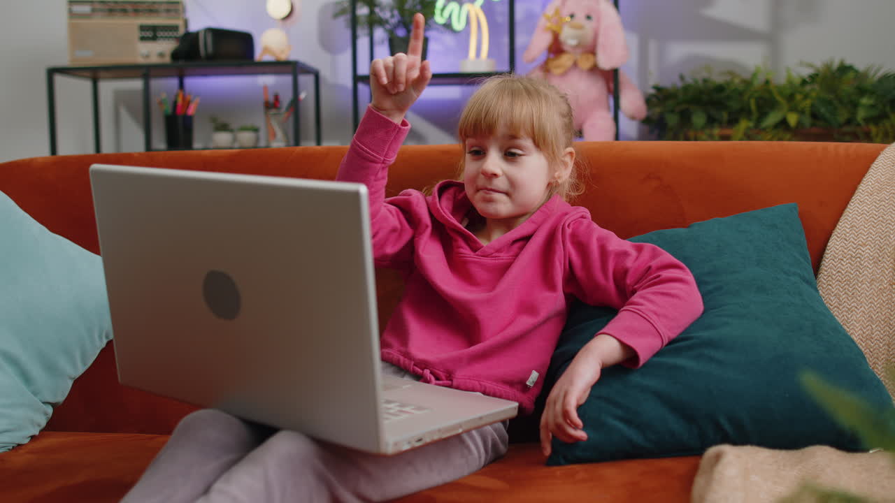 Overjoyed child kid girl with laptop play online game celebrate success win at home sits on sofa