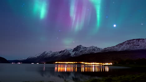 stunning vivid aurora borealis flaring in sky over snowy mountains, nightlapse