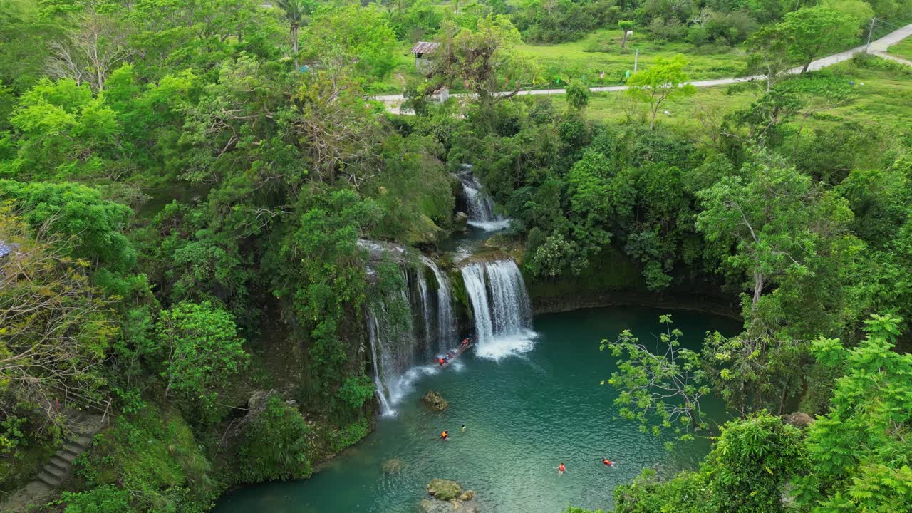 Ripresa aerea ascendente dall'alto delle Cascate di Bolinao a Pangasinan, Filippine, che rivela le cascate a più livelli e la vasta piscina naturale circolare color turchese circondata da una fitta vegetazione tropicale