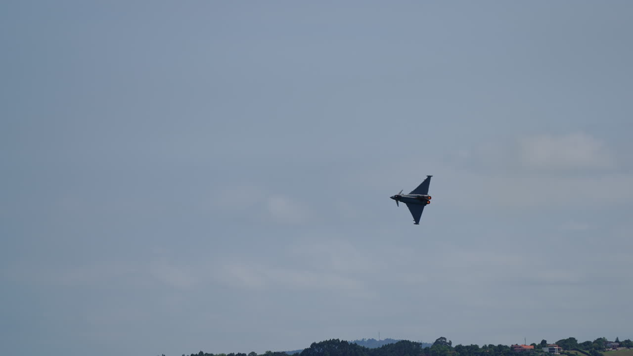 Military jet fighter flying at angle above lush green hills and residential area