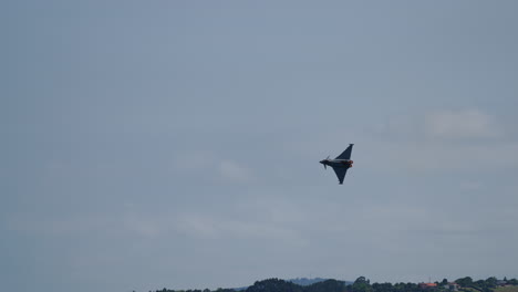 military jet fighter flying at angle above lush green hills and residential area