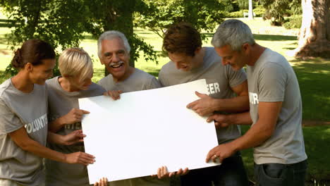 equipo de voluntarios felices en el parque mostrando un cartel