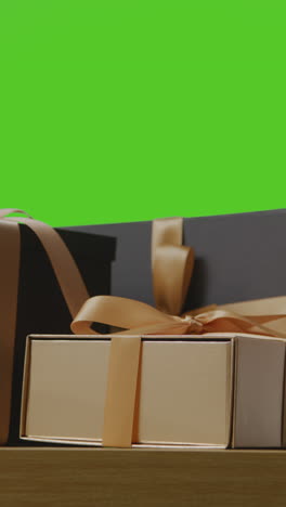 vertical video of man putting down present in gift wrapped box decorated with ribbon on table shot against green screen 1