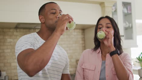 Happy-biracial-couple-drinking-self-made-smoothie-in-kitchen