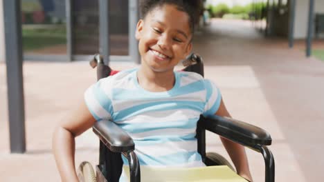 video portrait of smiling biracial schoolgirl in wheelchair in school corridor