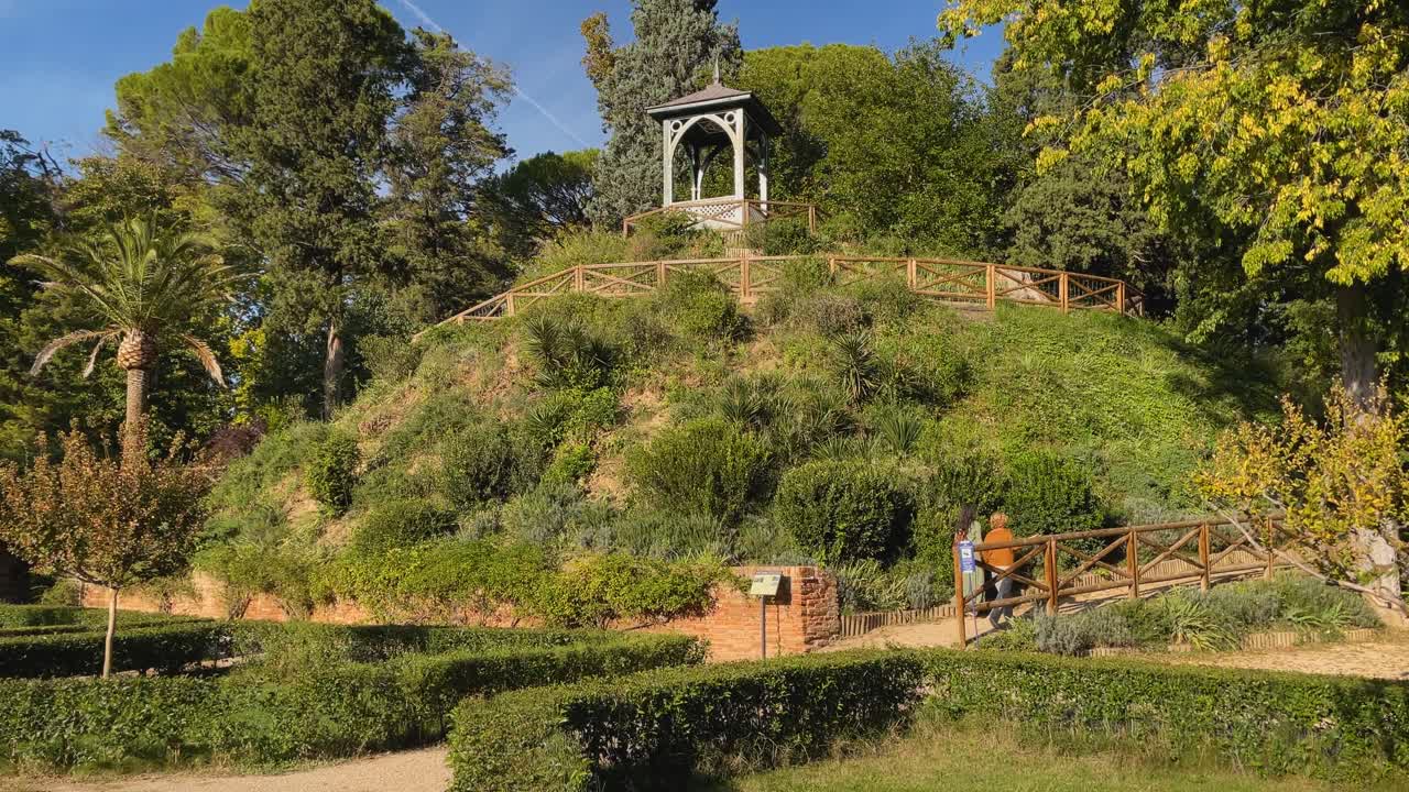 Slow motion filming of an area of ​​the Jardin del Principe called a roller coaster or Swiss coaster, it is a mound with a viewpoint at the top, it is accessed by going up in a spiral, 2 women go up