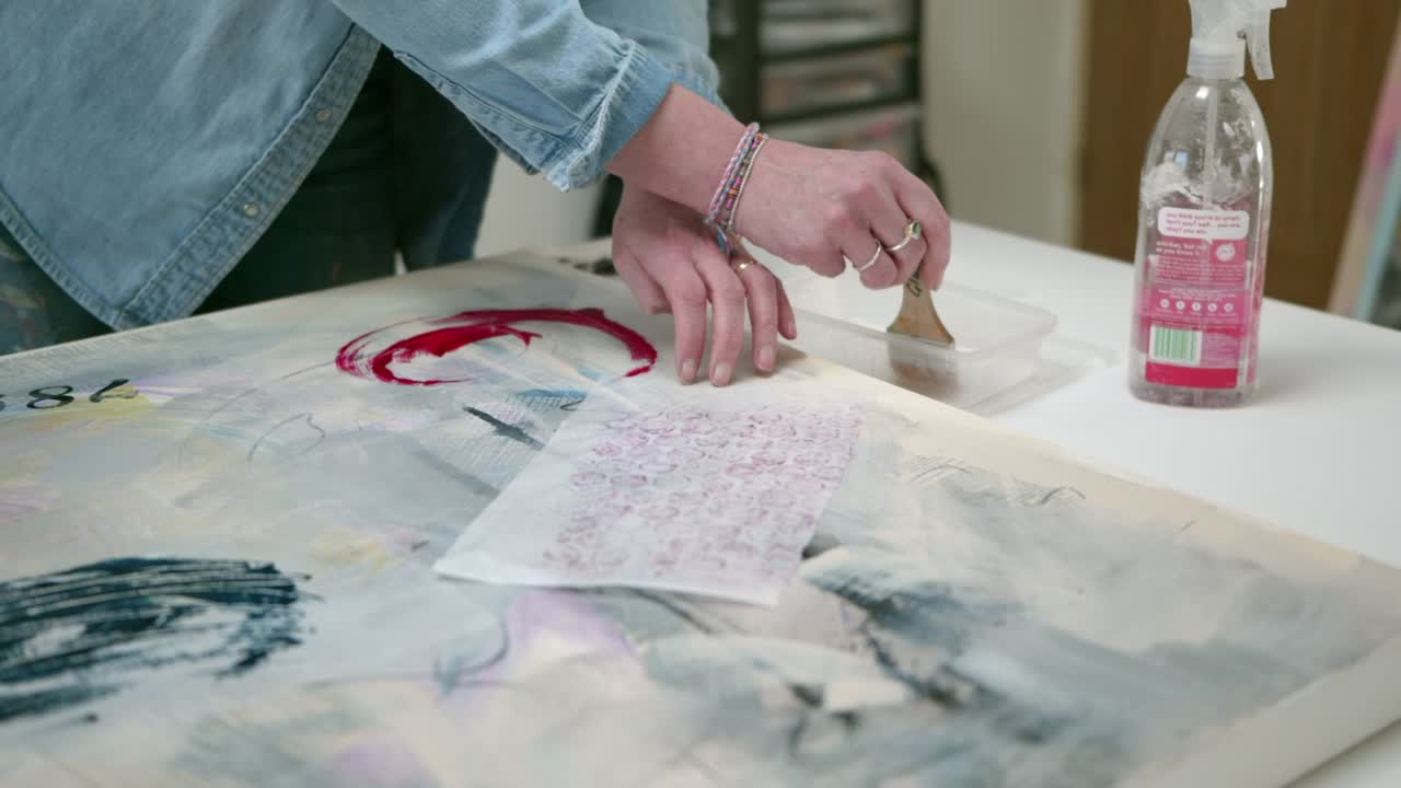 artista femenina cepillando pegamento en un activo de papel, en lienzo, en un estudio en casa