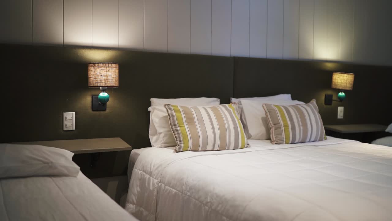 Moderne hotelværelse med en komfortabel seng med stribede puder, blød belysning og et minimalistisk design, der skaber en varm og indbydende atmosfære for gæsterne